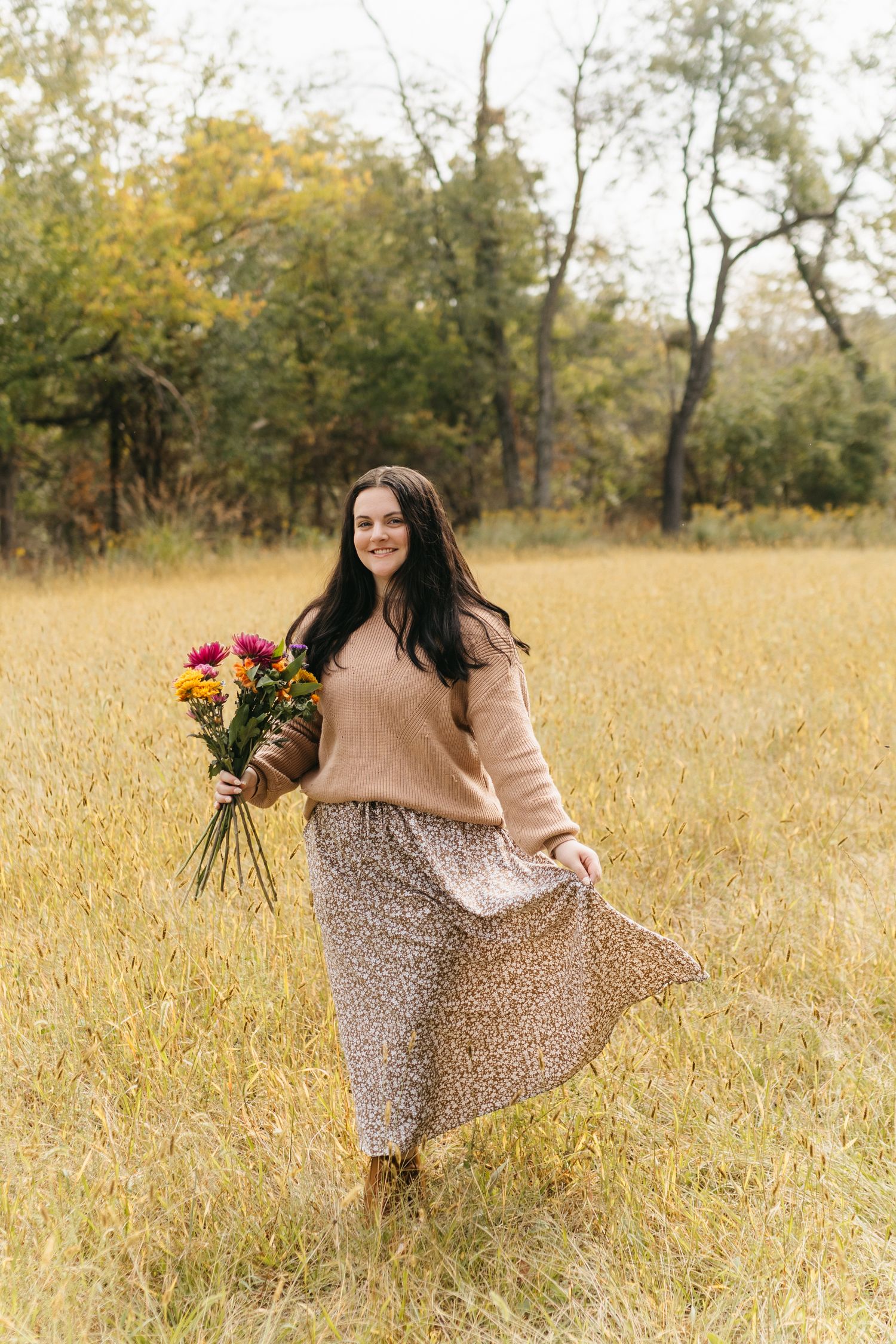 A floral dress twirls in a golden autumn field while holding colorful wildflowers.