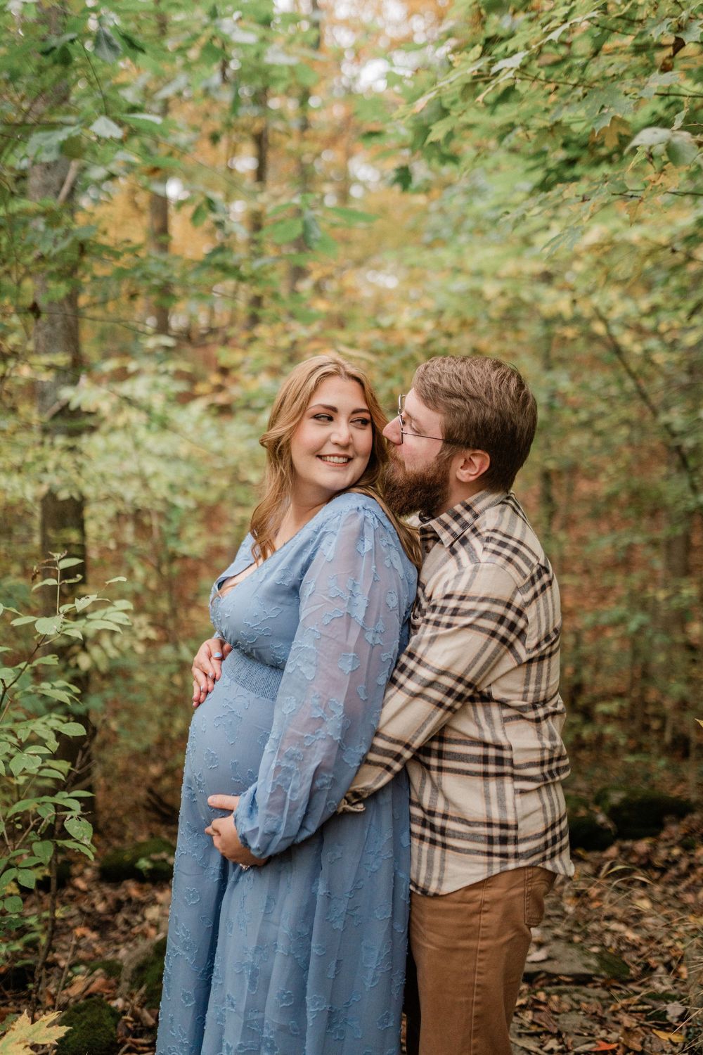 Expectant couple shares intimate moments during a fall photoshoot in a forest setting.