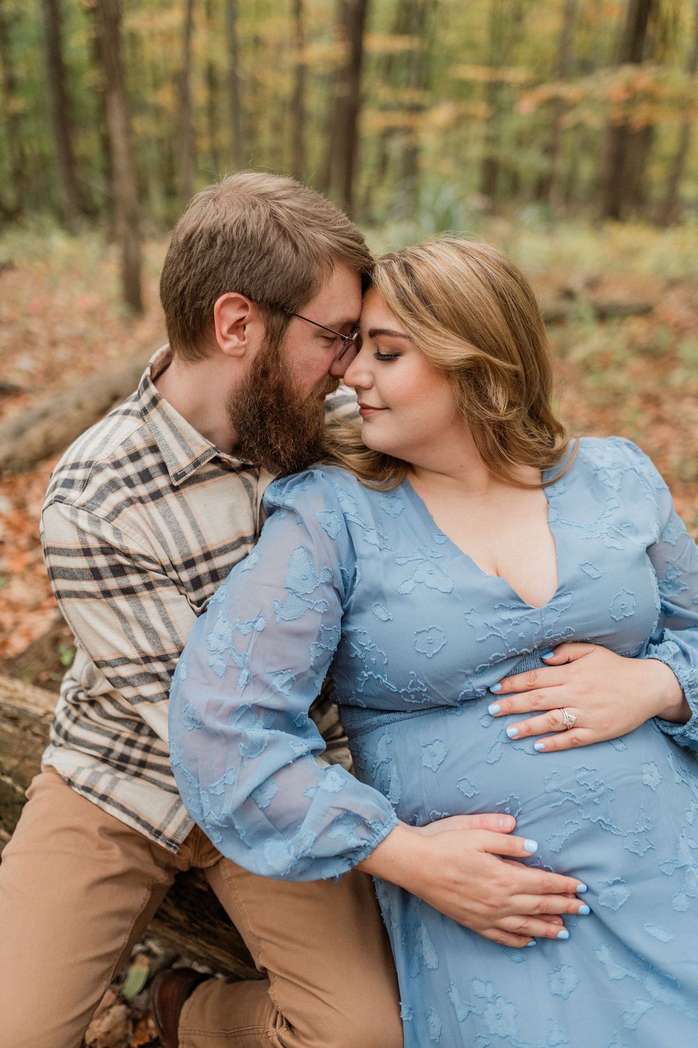 A tender embrace between a couple in autumn woods, with soft lighting filtering through the trees.