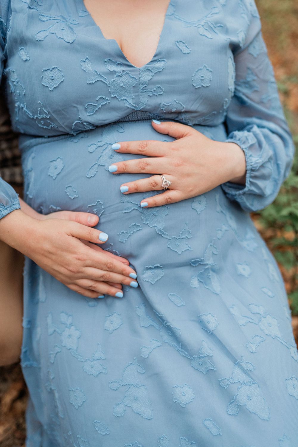 Close-up shots of hands gently cradling a pregnant belly wearing a soft blue textured dress.