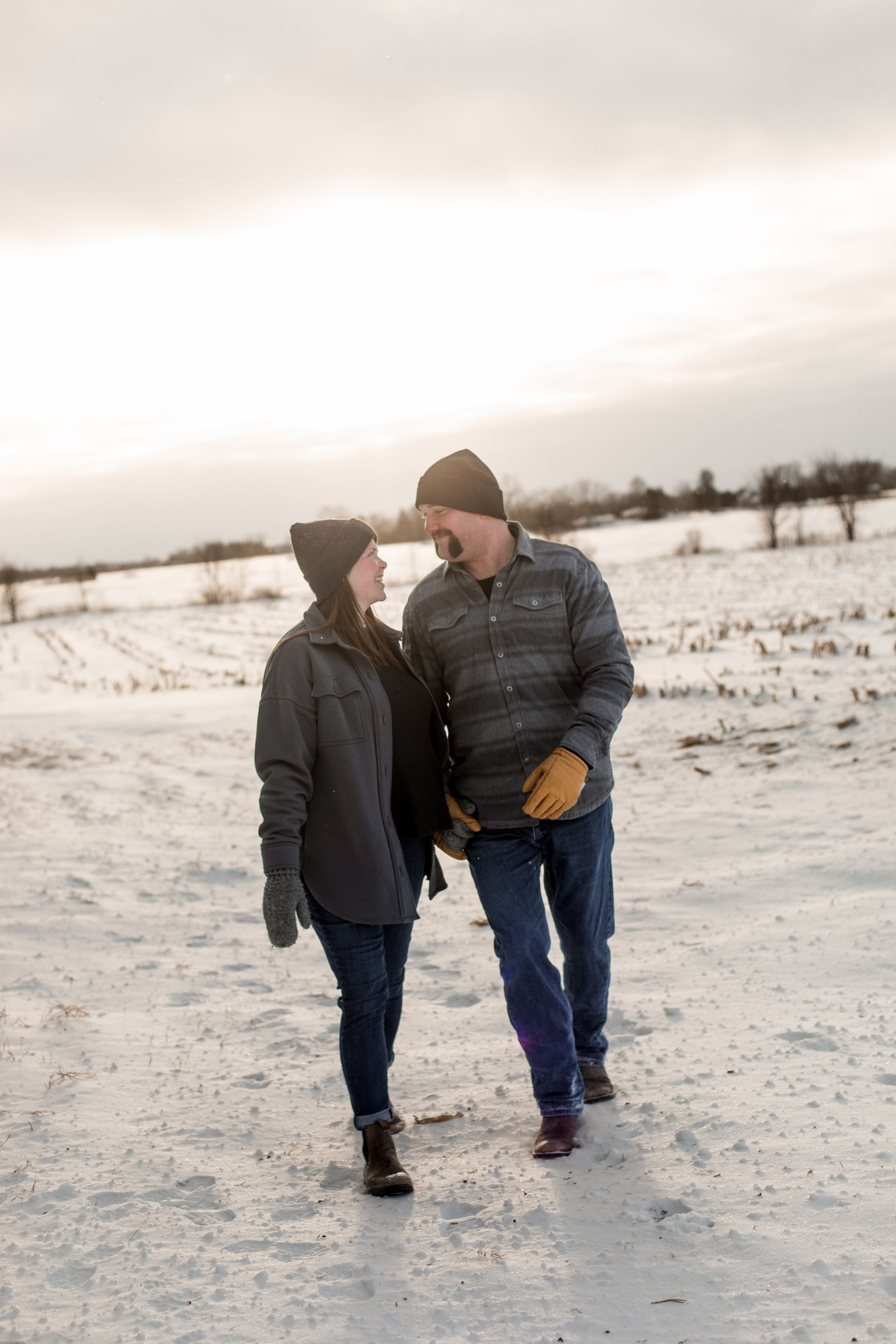 A couple shares a tender moment while walking together in a snowy winter landscape.