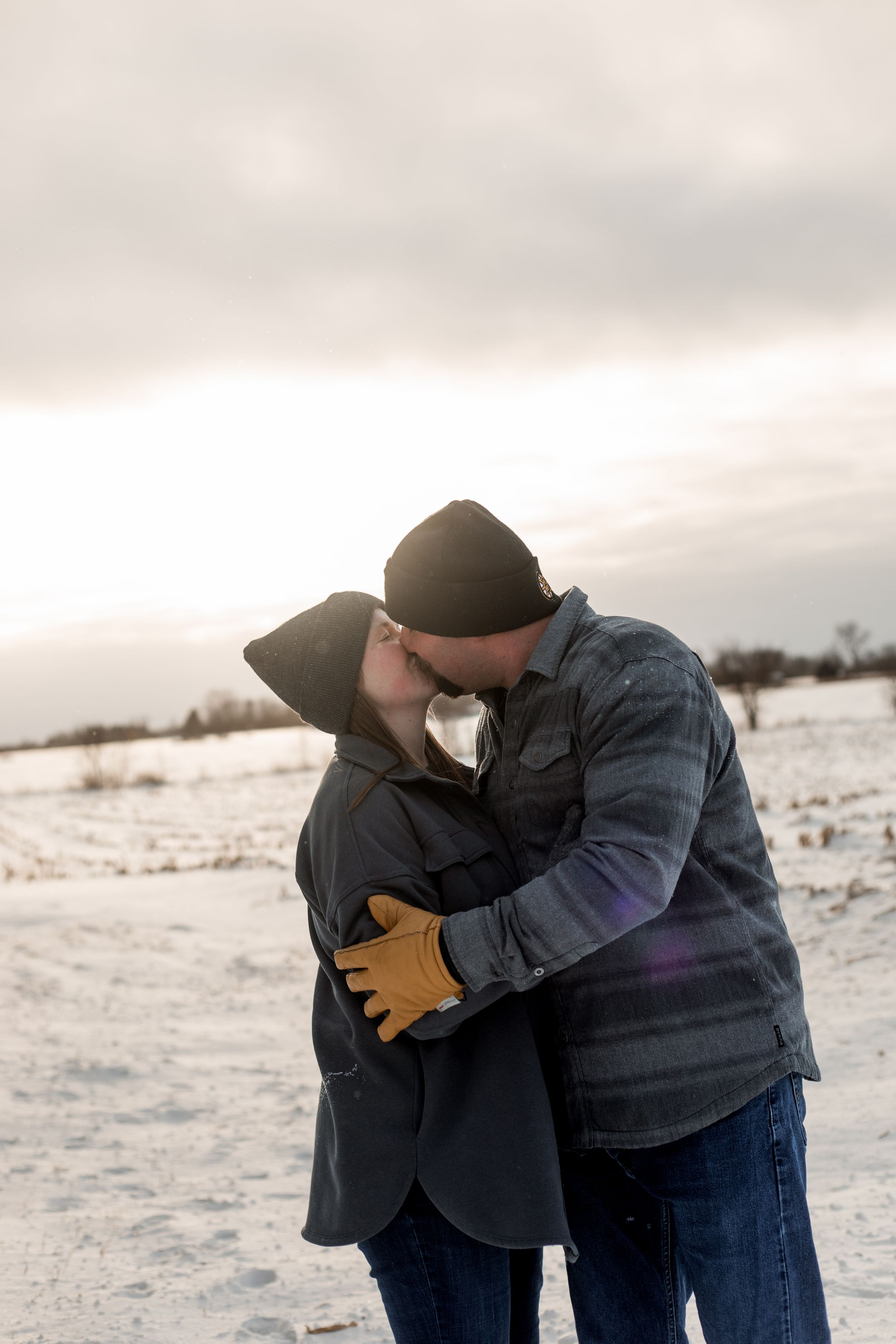 A couple embraces in a romantic moment on a snowy winter landscape during overcast weather.
