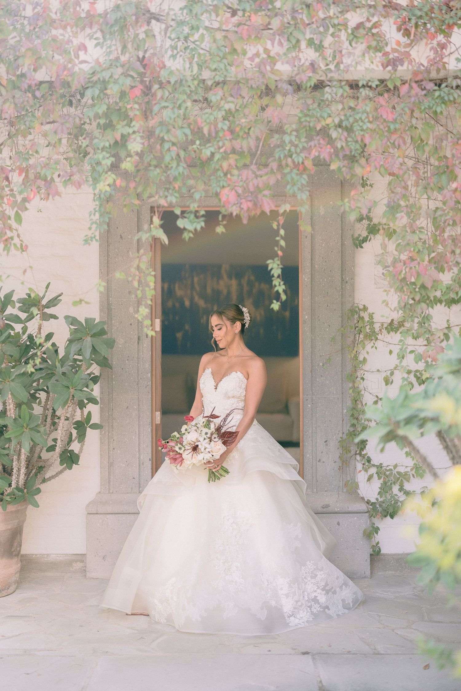 A romantic bridal portrait under an archway framed by delicate pink flowers and greenery.