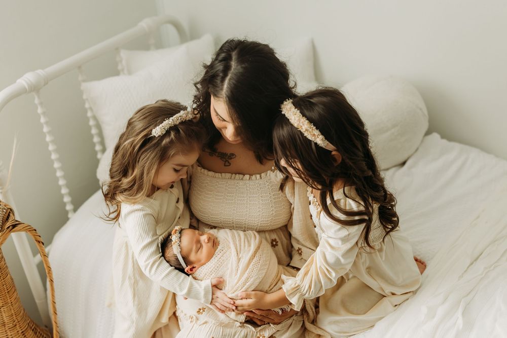 Mother and baby share tender moments together on white bedding in natural window light.
