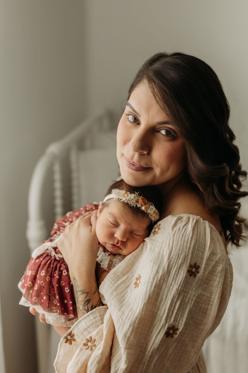 A tender portrait of a parent holding a sleeping newborn baby in a soft white dress.