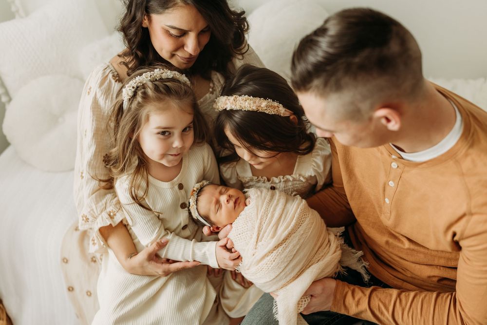 A family in warm earth tones gathers close together on a white couch for an intimate moment.