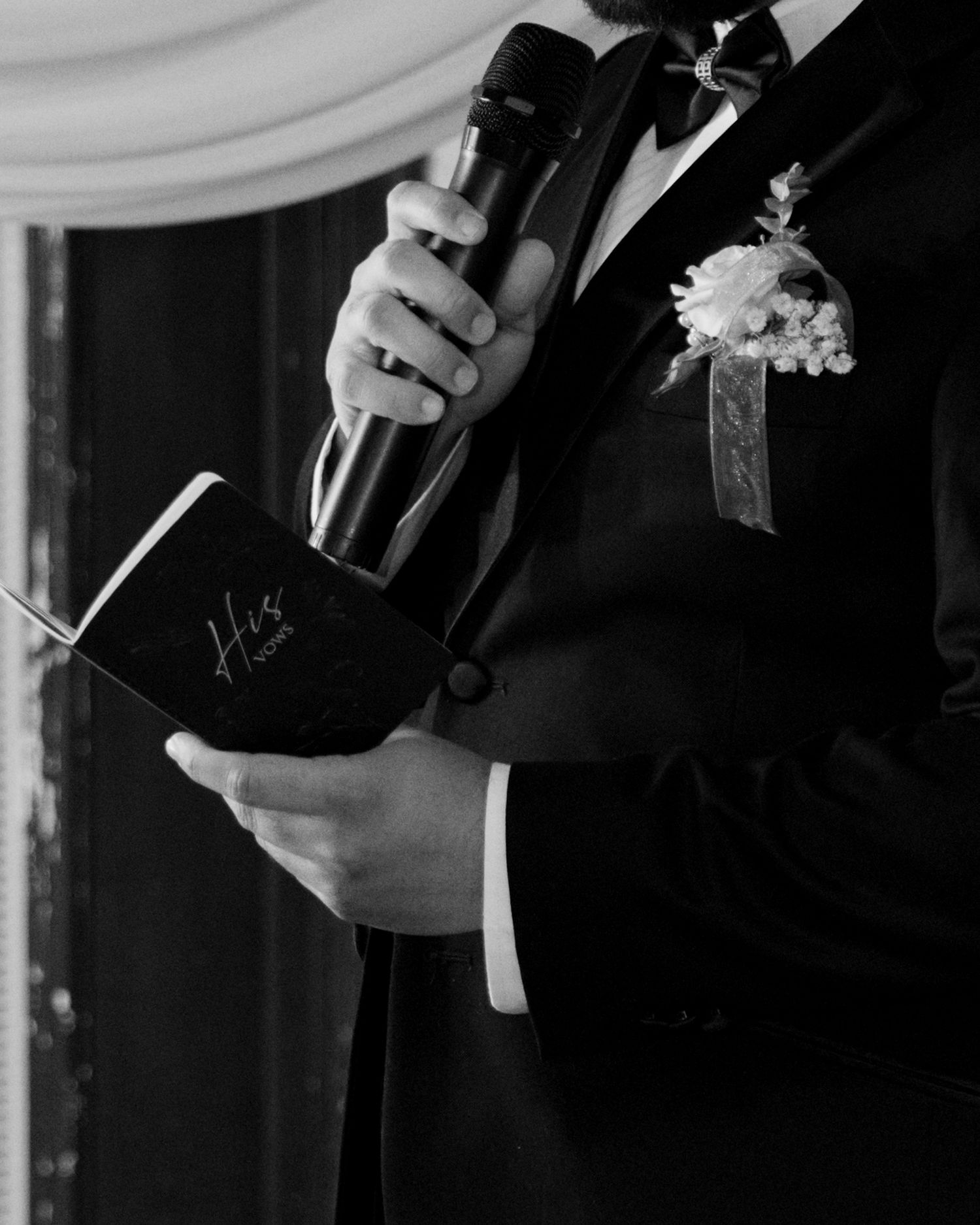 Black-and-white photo of the groom holding a microphone and wedding vows during the ceremony