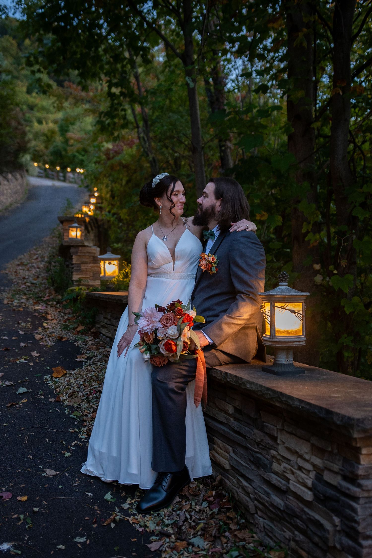 Romantic couple shares intimate moments at dusk by stone wall with glowing lanterns in autumn setting.