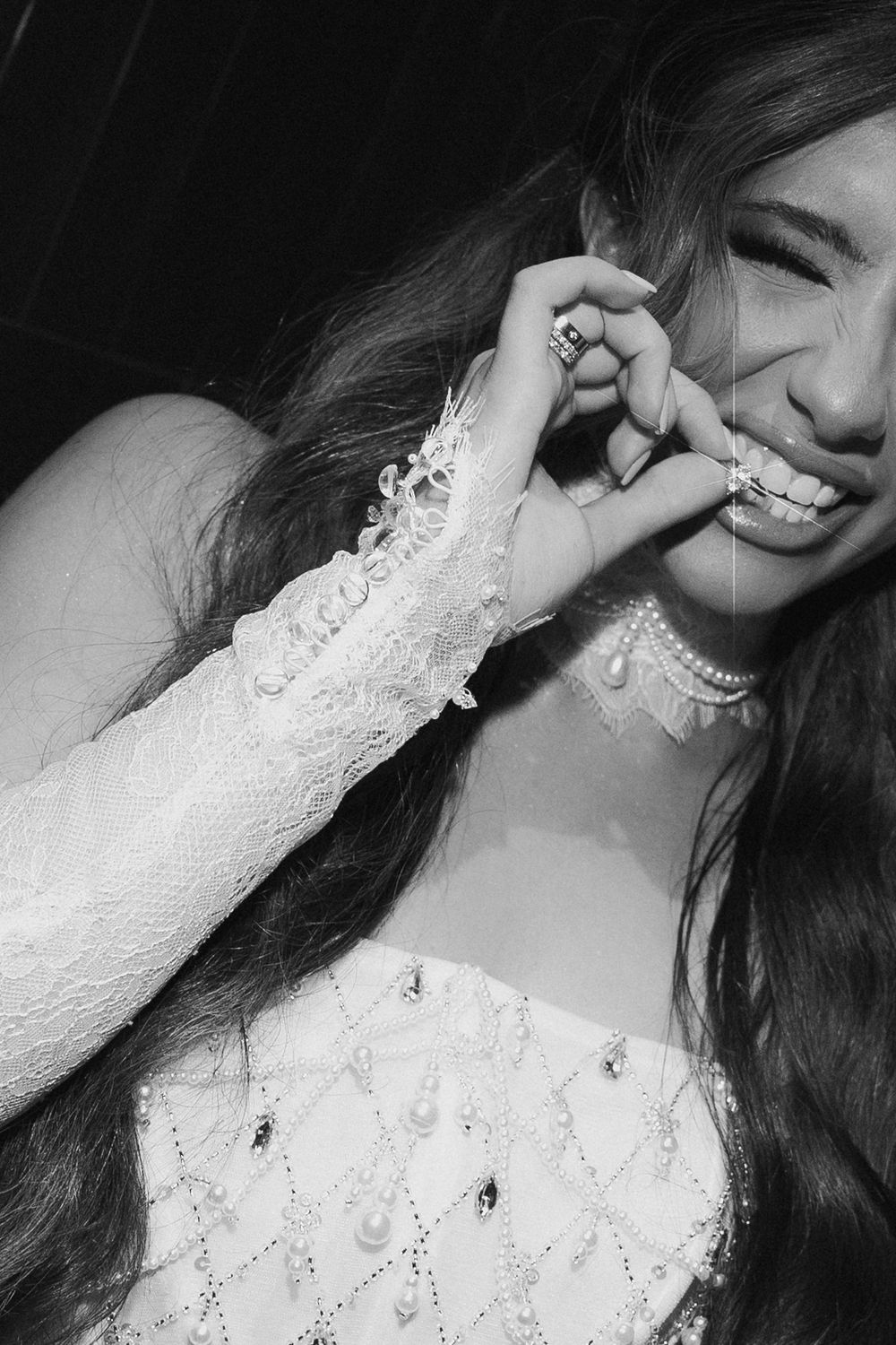 Black and white portrait of smiling bride in pearl-adorned wedding dress with long flowing hair.