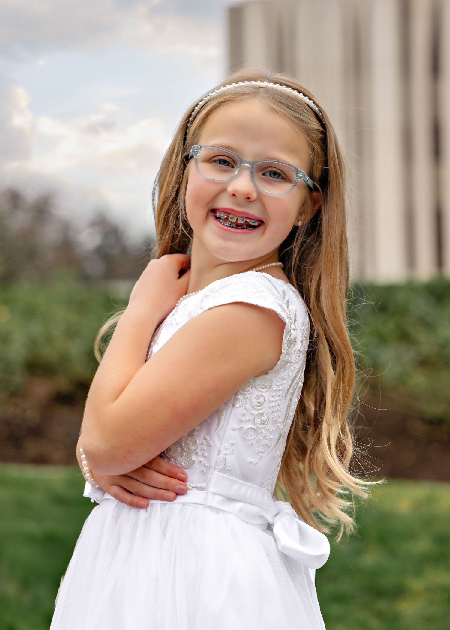 A young person in a white dress smiles and poses playfully in a series of outdoor portraits.