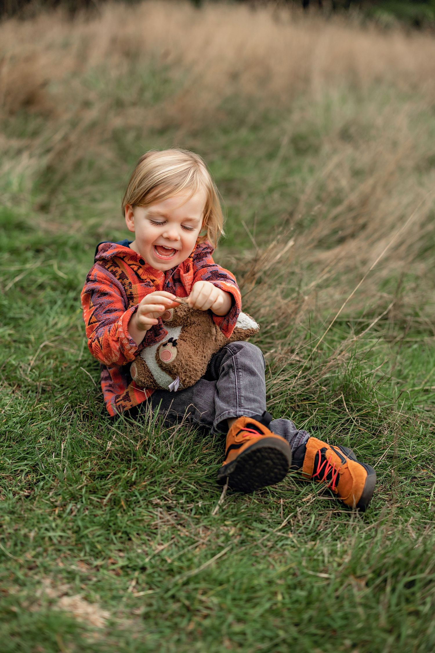 A child in an orange plaid shirt playing and laughing while lying in tall grass outdoors.