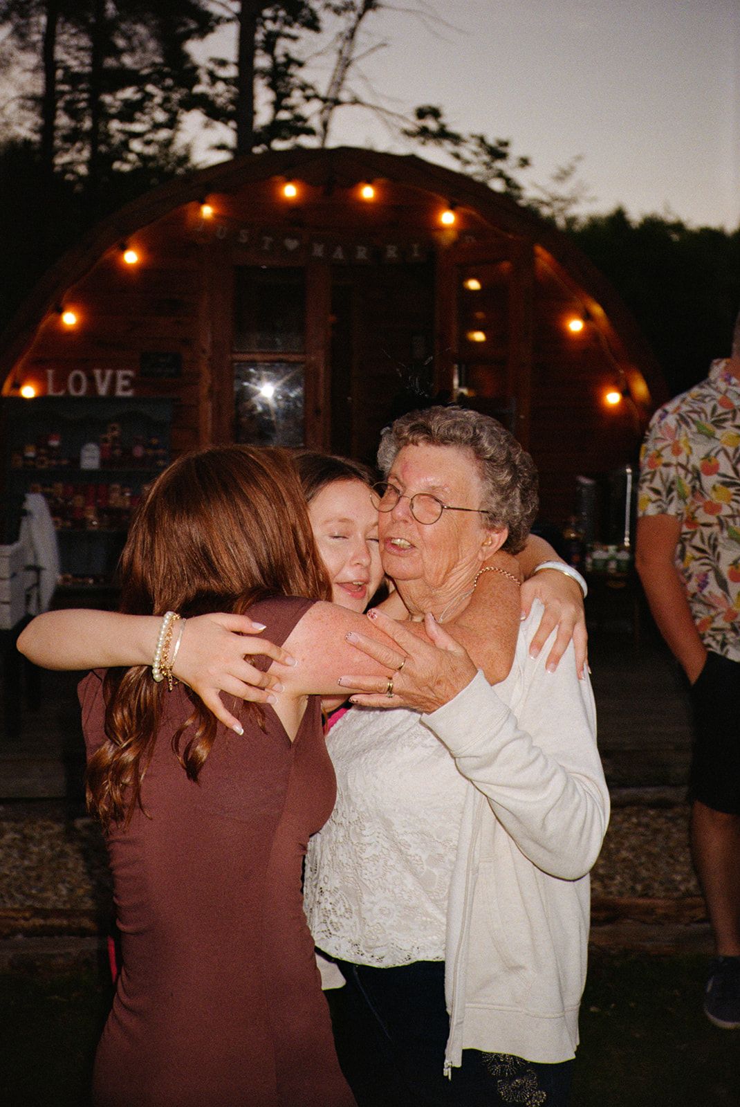 People dancing and embracing at an outdoor evening event with string lights glowing in the background.