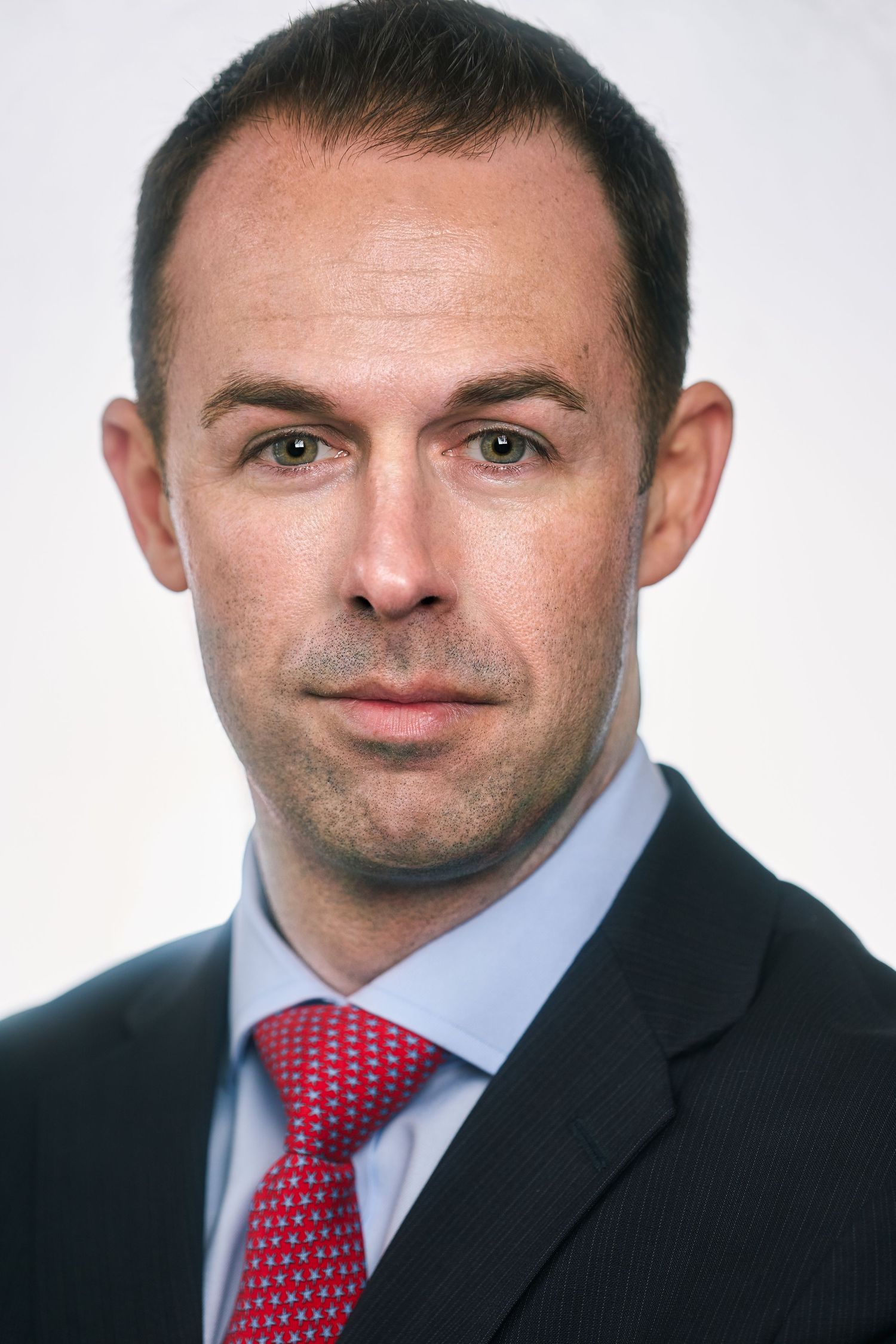 Professional businessman in dark suit and red tie with serious expression on white background.