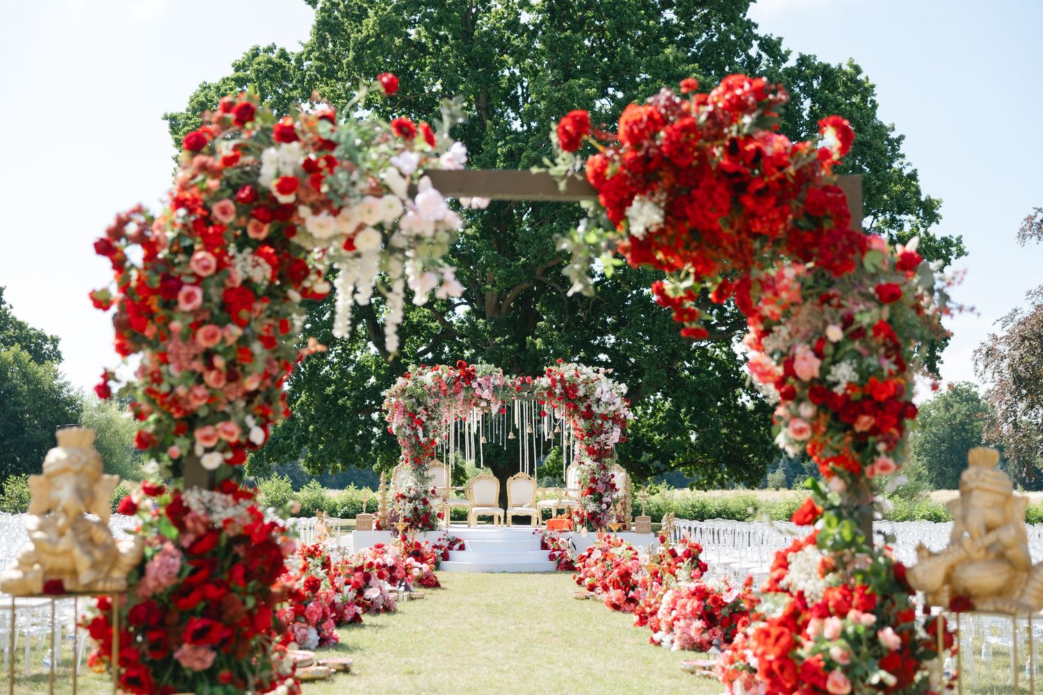 A stunning outdoor Hindu wedding ceremony setup featuring a grand floral mandap adorned with lush red and pink roses at Ditton Manor