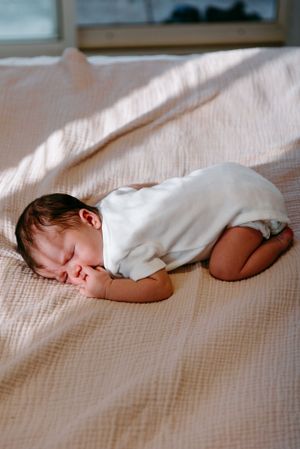 Peaceful baby napping in white onesie on soft textured bedding.