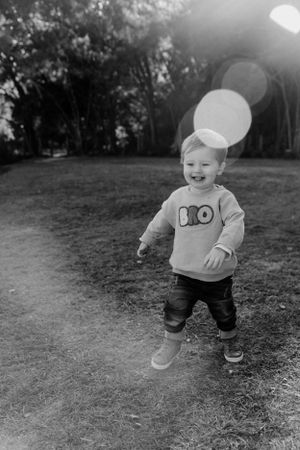 Joyful toddler in grey sweater playing outdoors with lens flare effect.