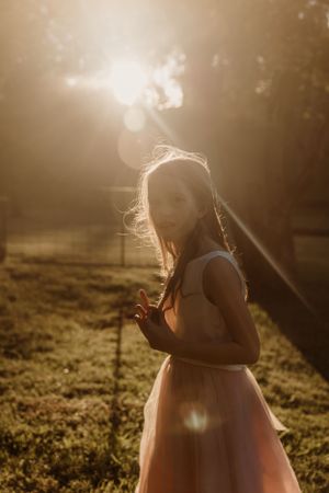 Person in a sleeveless dress twirling in dreamy golden sunset light in a grassy field.