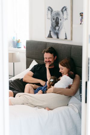 Family relaxing in bed with koala artwork visible on wall above.