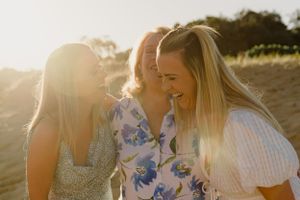 Two women sharing a laugh in golden sunlight outdoors.