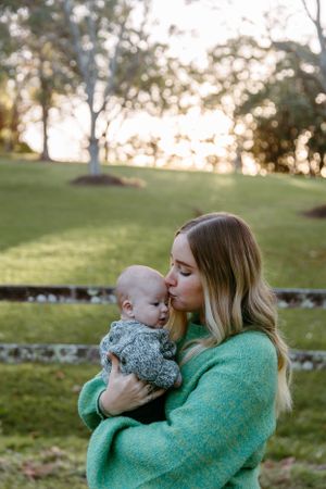 Person in green sweater cradles infant outdoors during golden hour.