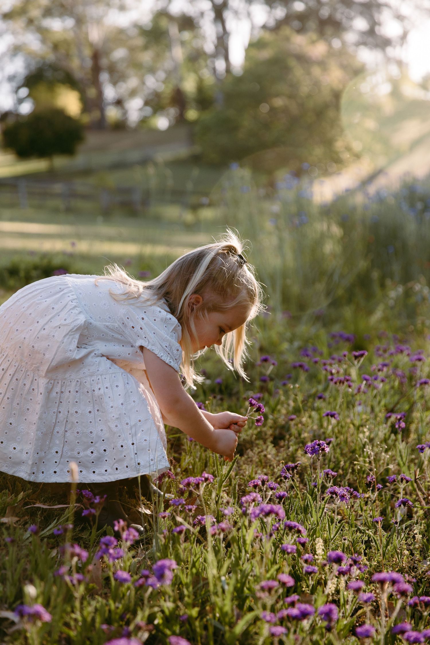 Person in white dress bending to pick flowers in a blooming spring garden.