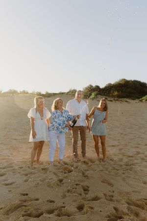 Group portrait on sandy beach during sunset with soft golden lighting.