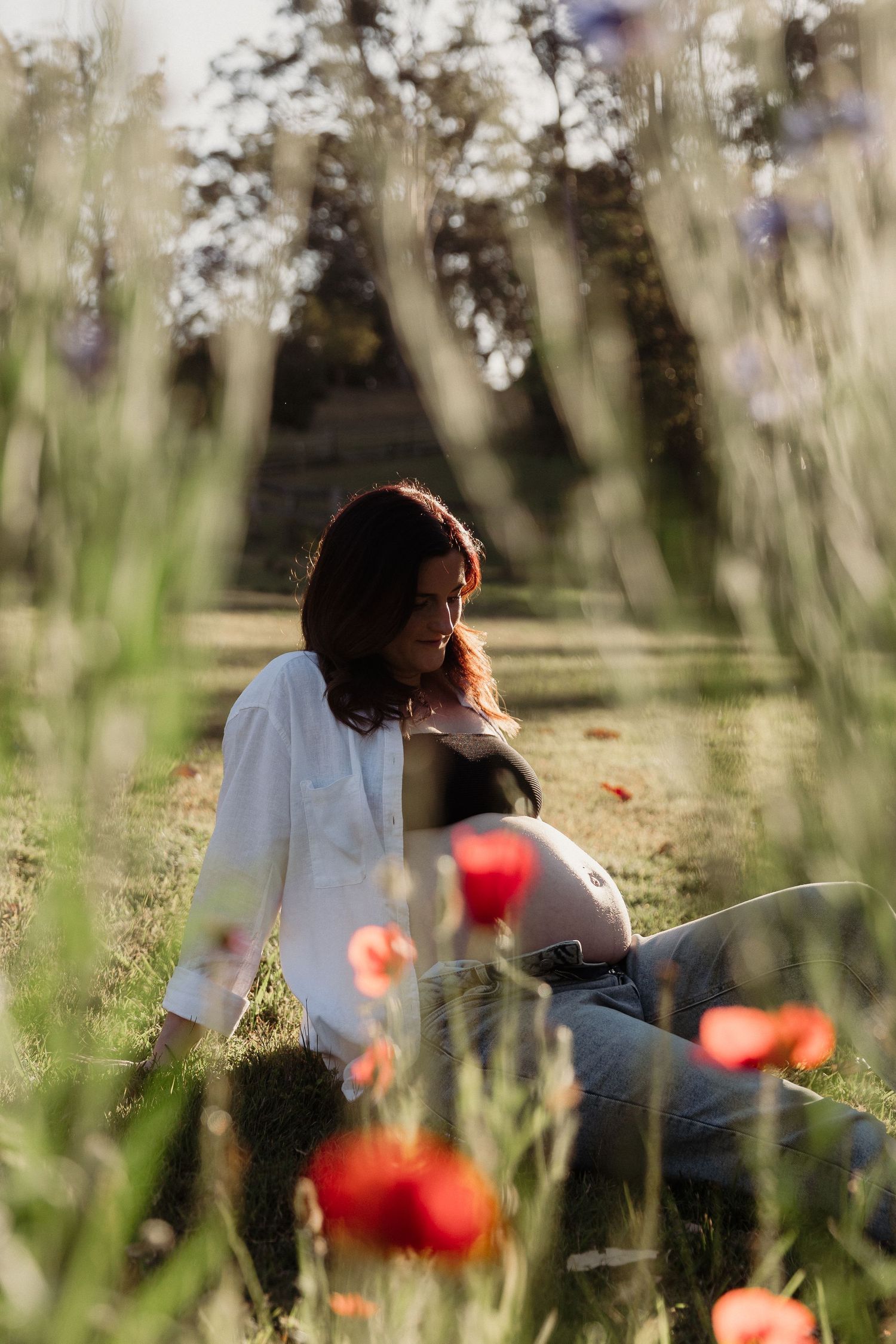 Person sitting among red poppies and wildflowers in dreamy afternoon light.