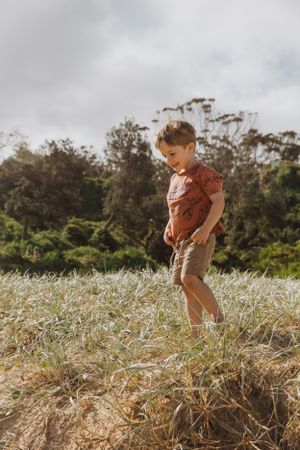 Child playing outdoors in a grassy field with eucalyptus trees in the background.