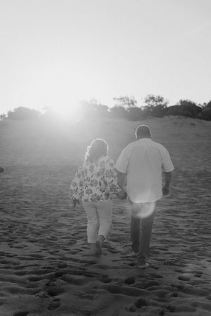 Black and white image of couple walking on beach at sunset.