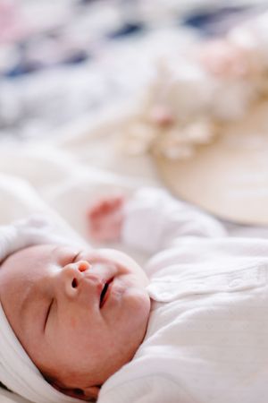 Close-up of sleeping infant in white clothing on soft bedding.