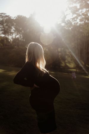 Silhouette of pregnant woman in black dress against sunset in park.