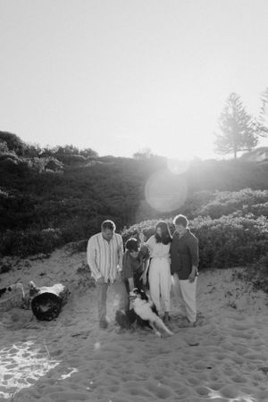 A group poses with their dog on a sandy beach during sunset at dusk.