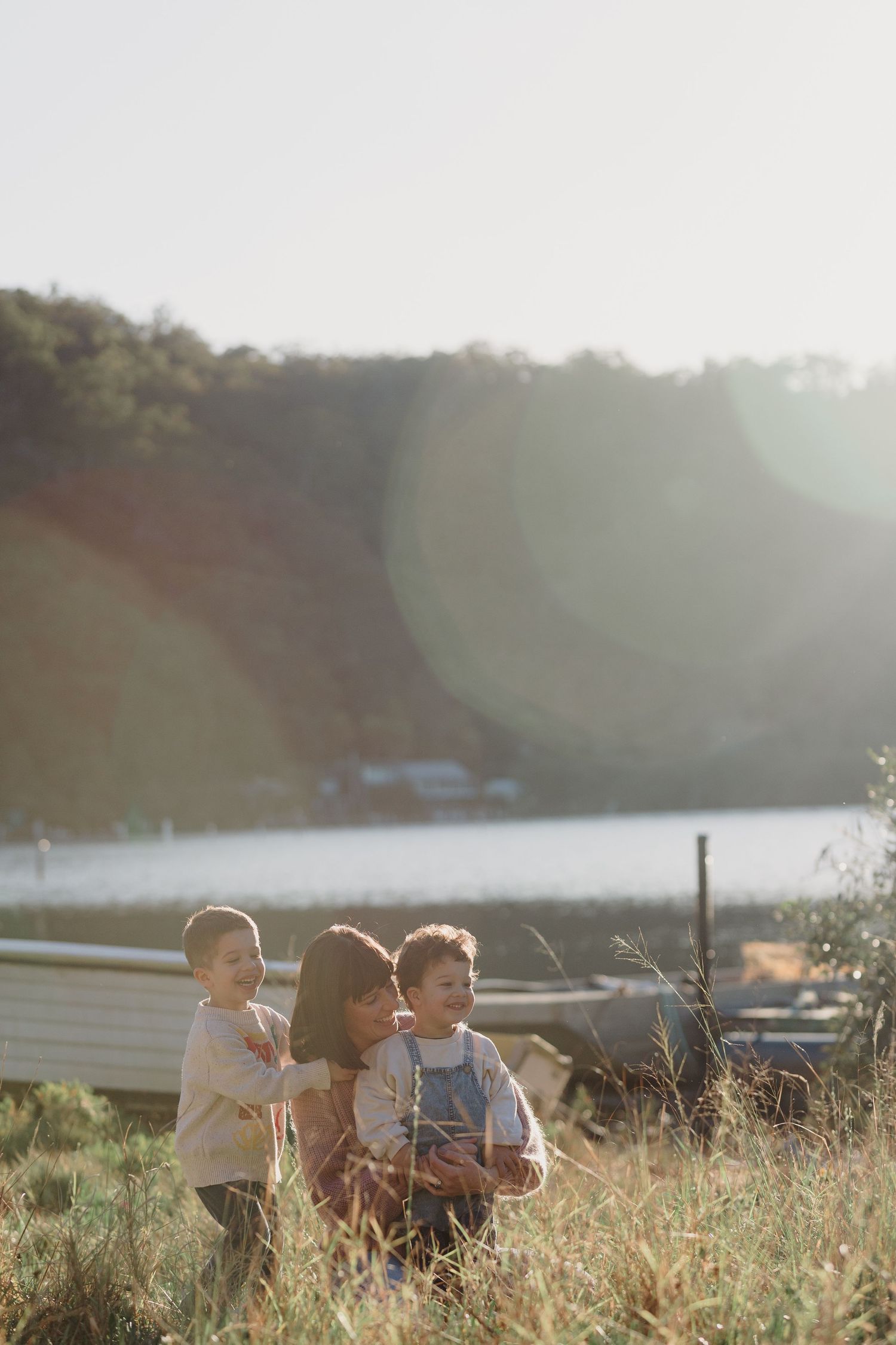 Children playing together in tall grass on a hillside during sunset with a lake in the background.