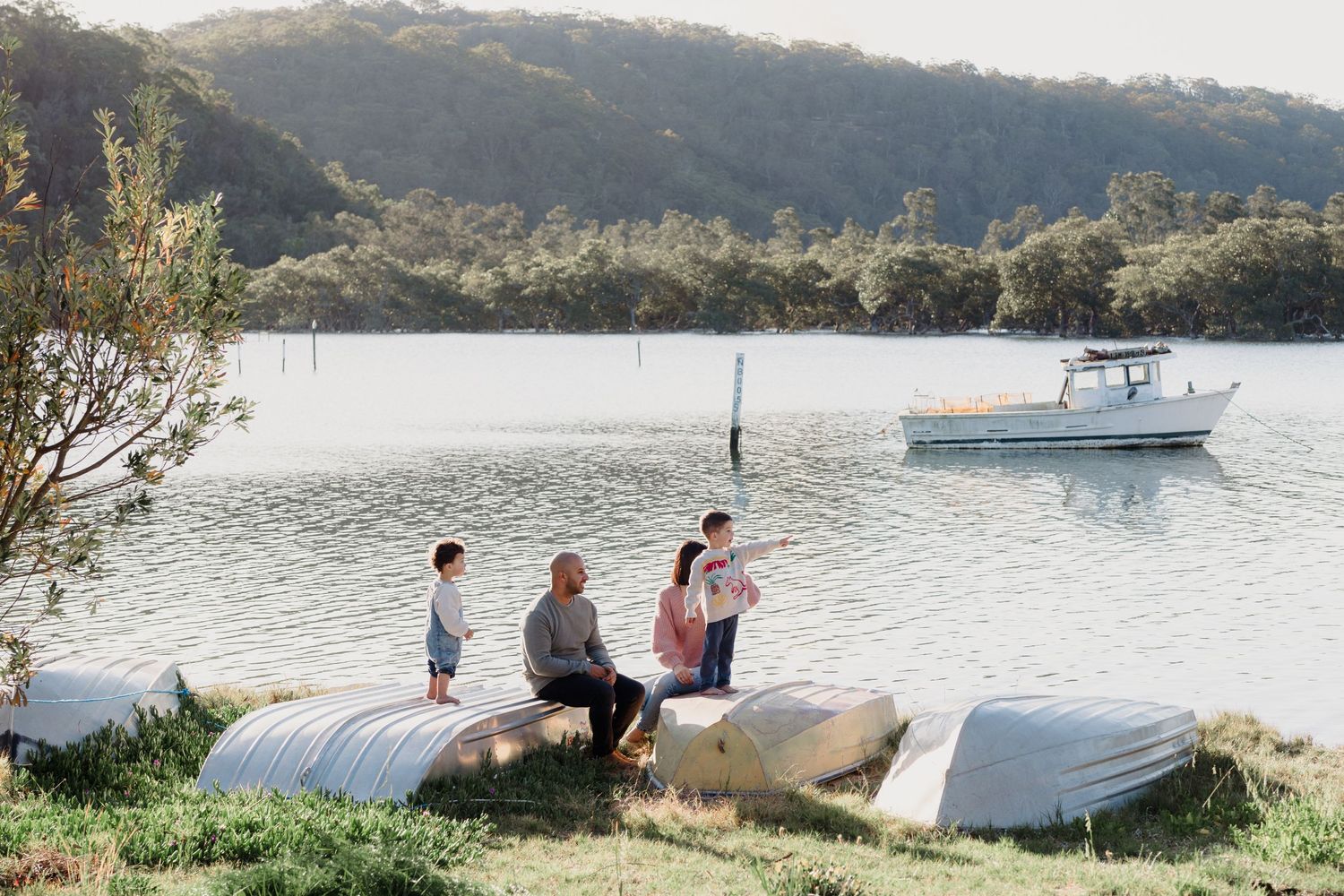 Family relaxing near boats by the waterfront on a sunny afternoon.