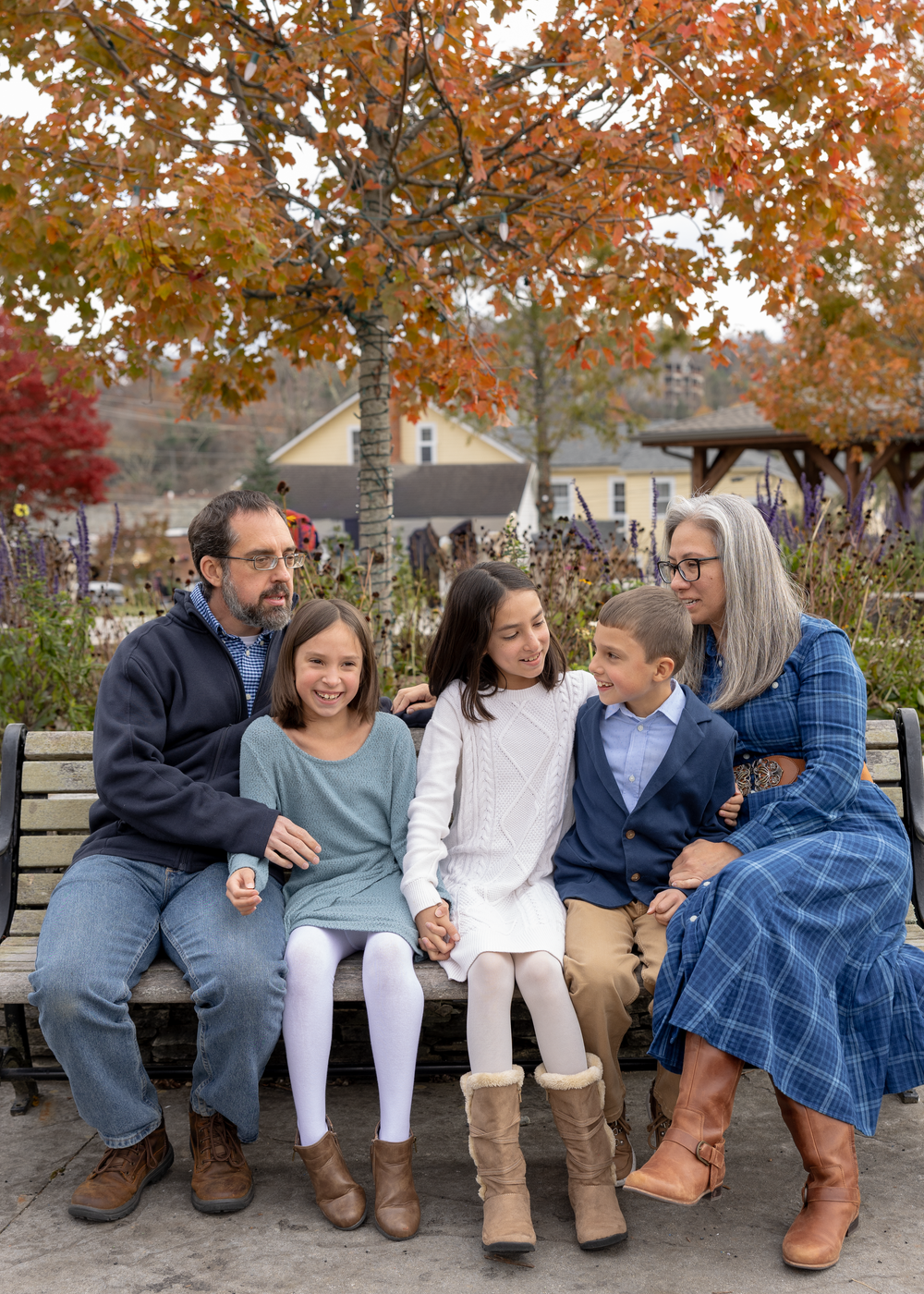 A family of five sits together on a bench surrounded by colorful autumn foliage.