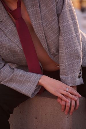 Close-up detail of hands resting on concrete while wearing a plaid blazer.