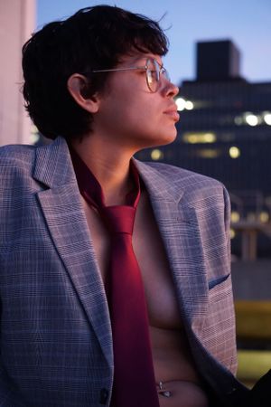 Person in plaid blazer and burgundy shirt gazing thoughtfully at sunset.