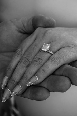 Black and white close-up of hands with engagement ring and manicured nails.