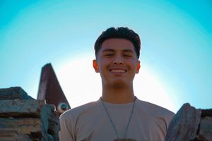 Person smiling against a bright blue sky backdrop in an outdoor setting.