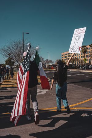 Group of protesters holding American flags and signs on a street during daytime.
