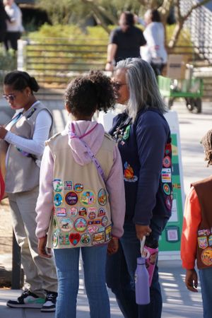Group of people wearing vests covered in colorful patches and badges standing in line outdoors.