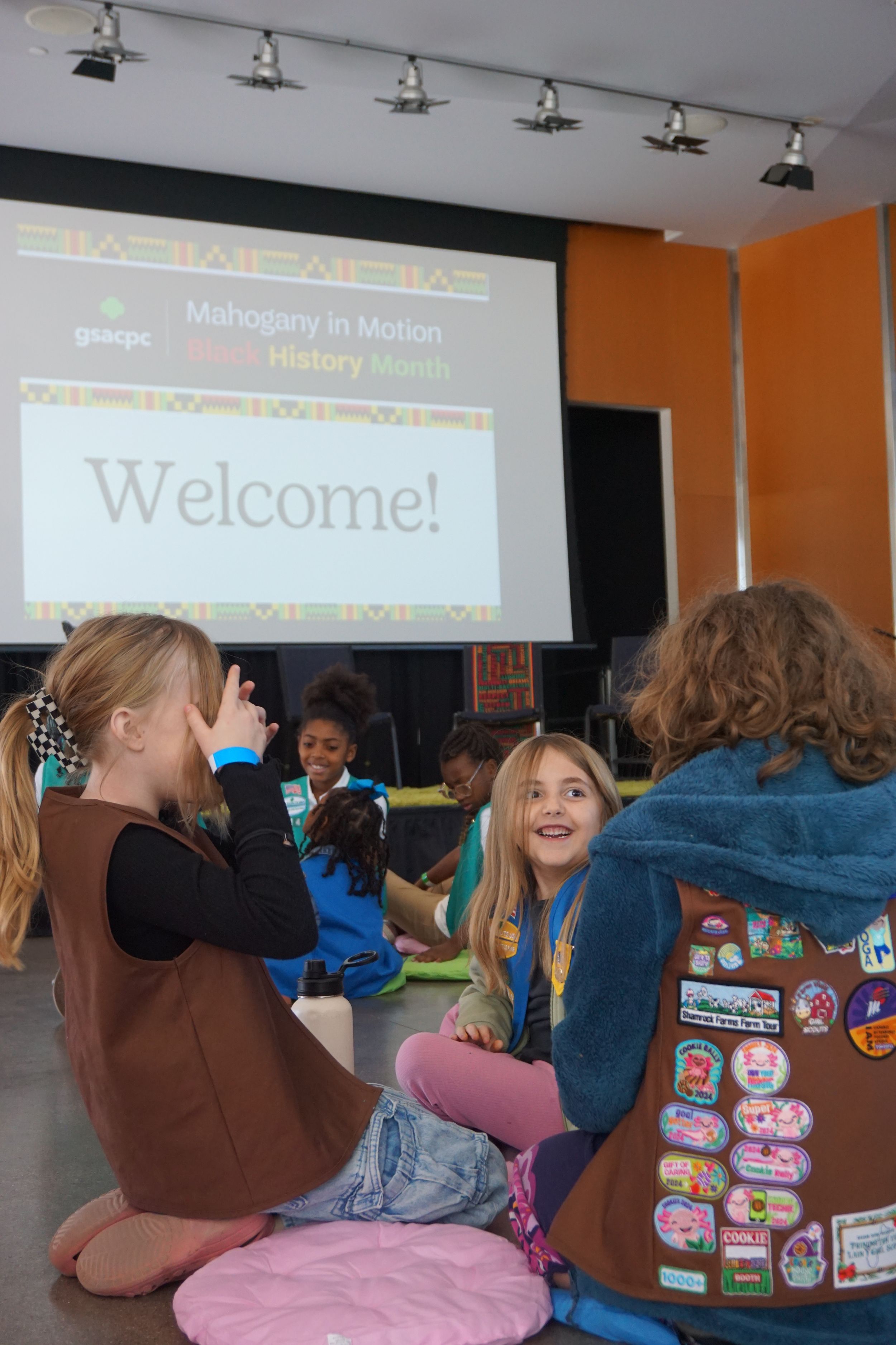 Students wearing scout badges watch a presentation in a classroom with projected screens.