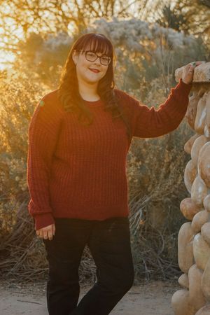 Person in red sweater and black pants posing by white pumpkins at sunset.