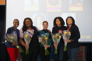 Group photo of people holding flower bouquets at an awards ceremony.