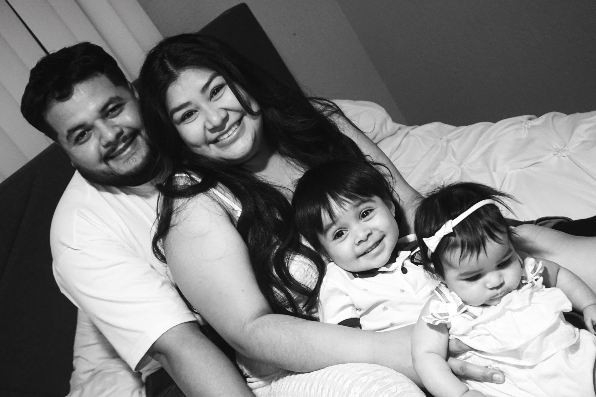 Family members share an intimate black and white moment together on a bed.