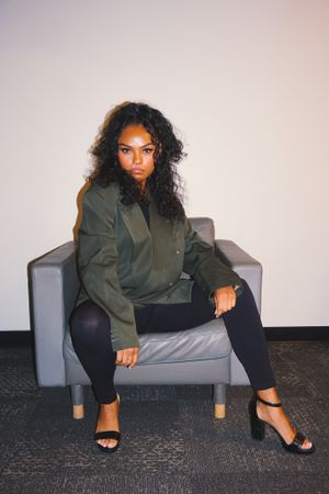 Person in olive green jacket lounging on grey couch during photo shoot.