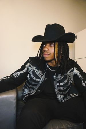 Person in black wearing a cowboy hat and patterned scarf lounging on a couch.