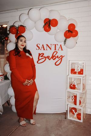 Holiday-themed maternity photo setup with red and white balloon arch and decorative boxes.
