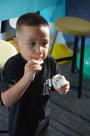 Child in black shirt enjoying an ice cream treat indoors.