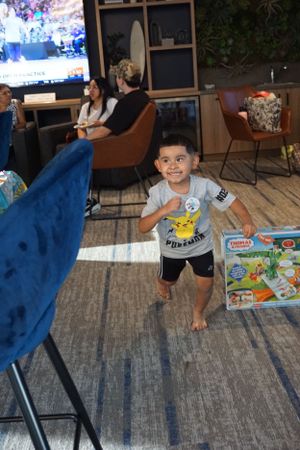 Living room setting with people watching TV and a child playing on a patterned rug.